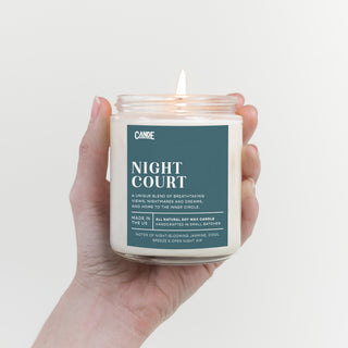 Hand holding a candle labeled 'Night Court' against a light background